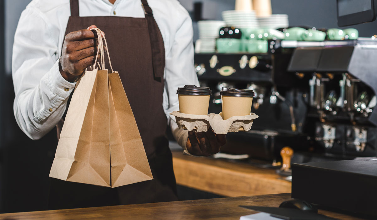 A Restaurant Worker Hands A Customer A Bag Of Food