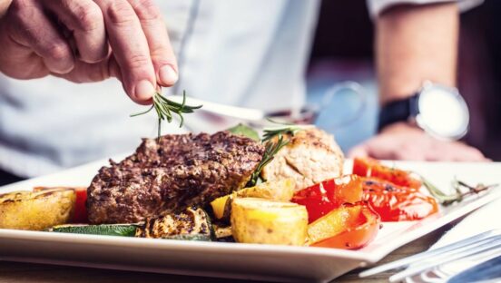 Chef in hotel or restaurant kitchen plating a steak.