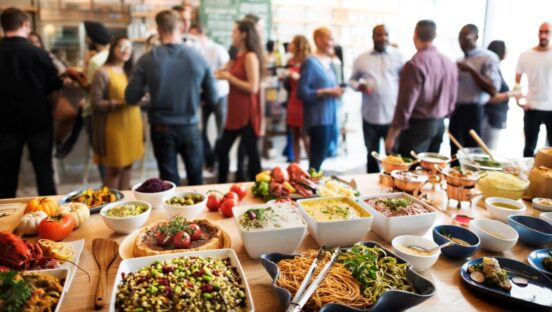 Catering table full of food with a party going on in the background.