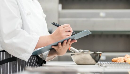 Restaurant chef checking for food safety on a clipboard in the kitchen.