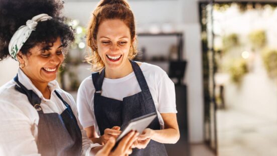 Two restaurant employees looking at a tablet and laughing.